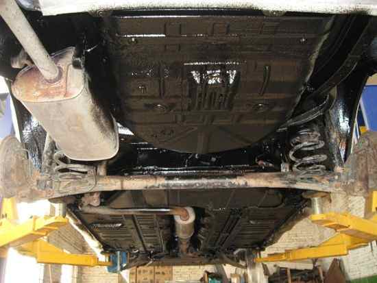 Нанесение мастики на днище автомобиля человеком в защитной маске